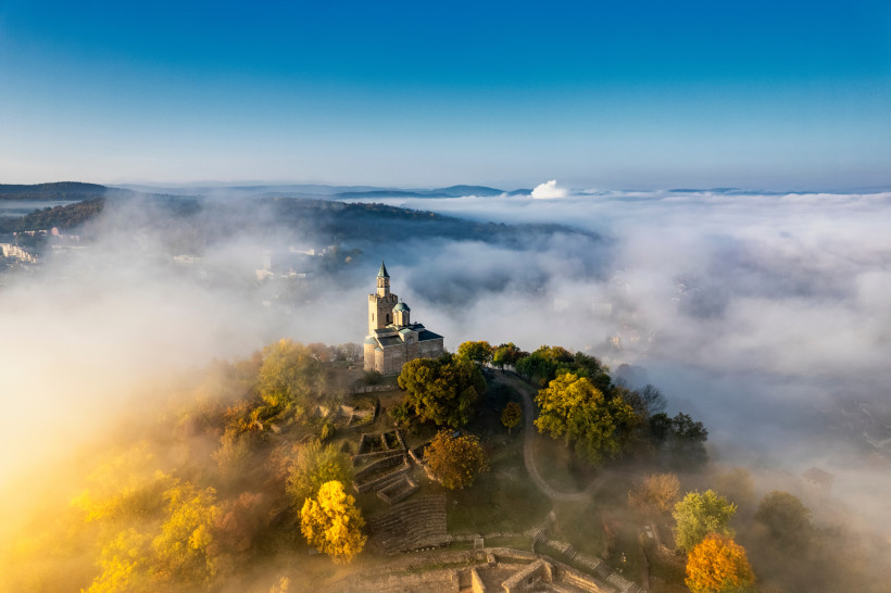Bulgarien Alte Burg auf einem Hügel umgeben von buntem Herbstlaub, eingetaucht in dichte Nebelschwaden, mit klar blauem Himmel darüber