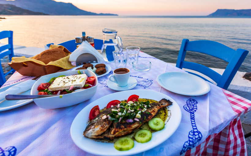 Griechische Speisen am Tisch am Meer mit gegrilltem Fisch, Salat und Brot