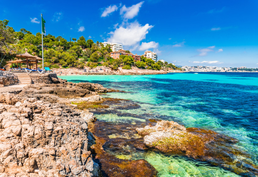 Blick auf die Bucht Cala Comtesa mit Felsufer, türkisblauem Meer und Häusern am bewaldeten Hang