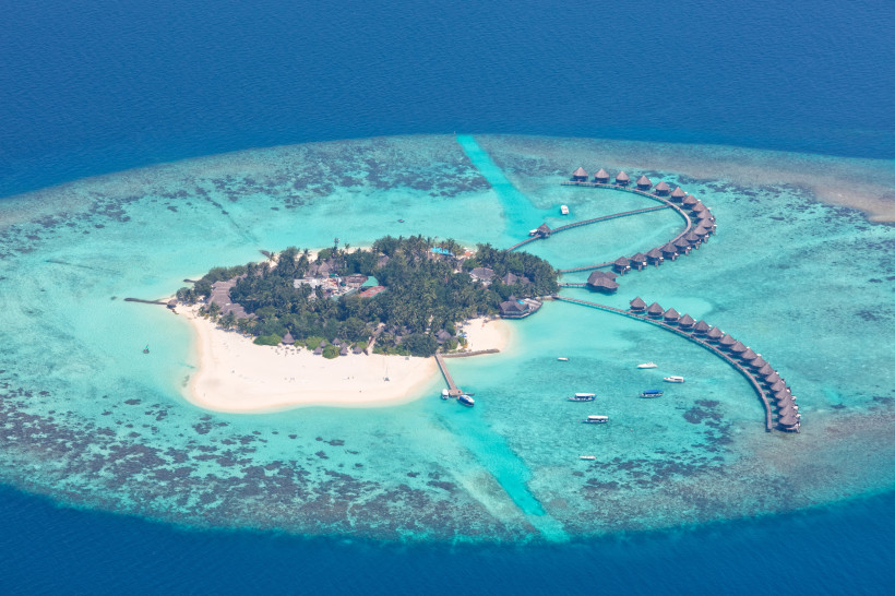 Malediven - Raa-Atoll Luftaufnahme einer Malediven-Insel mit weißen Sandstränden, türkisblauem Wasser und Wasserbungalows, die halbkreisförmig ins Meer gebaut sind.