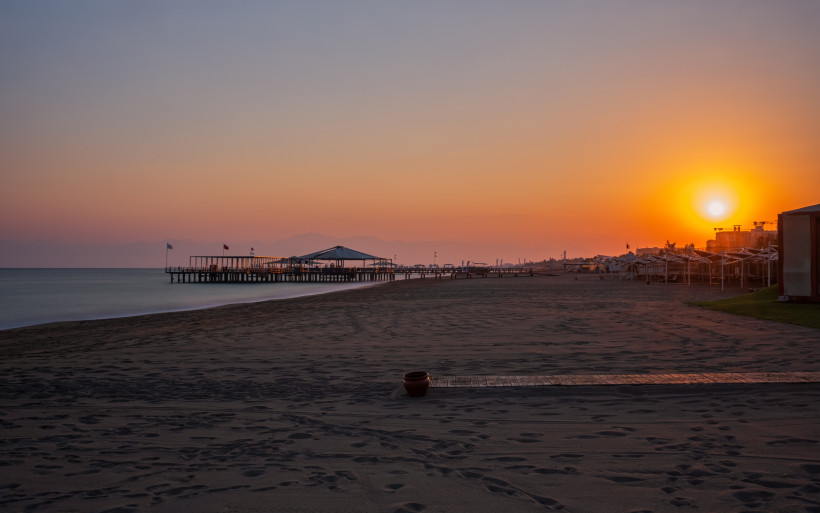 Belek Zentrum Strand bei Sonnenuntergang – Pier Sonnenuntergang am Strand von Belek Zentrum mit langem Holzsteg, ruhigem Meer und Hotelbereich der Türkischen Riviera