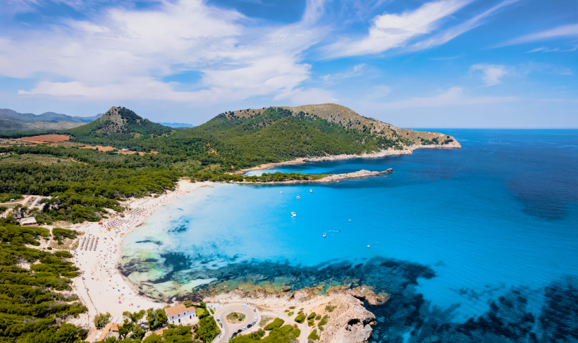Cala Agulla: Bucht mit Sandstrand und klarem, türkisblauem Meer Blick über die Cala Agulla mit Sandstrand, türkisblauem Wasser und bewaldeten Hügeln im Hintergrund