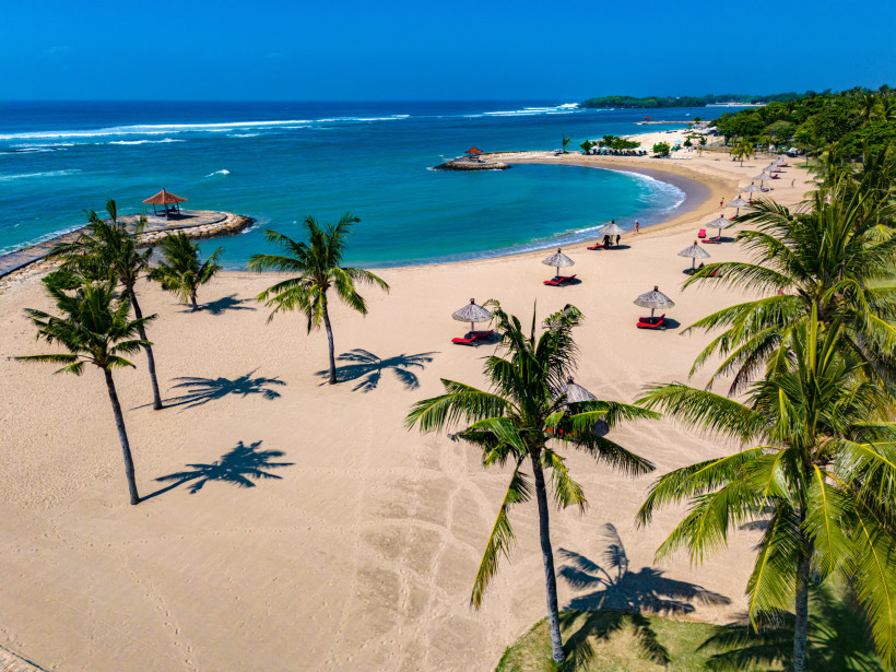 Nusa Dua, Bali Tropischer Strand in Nusa Dua, Bali, mit Palmen, weißen Sonnenschirmen und ruhigem türkisblauen Meer