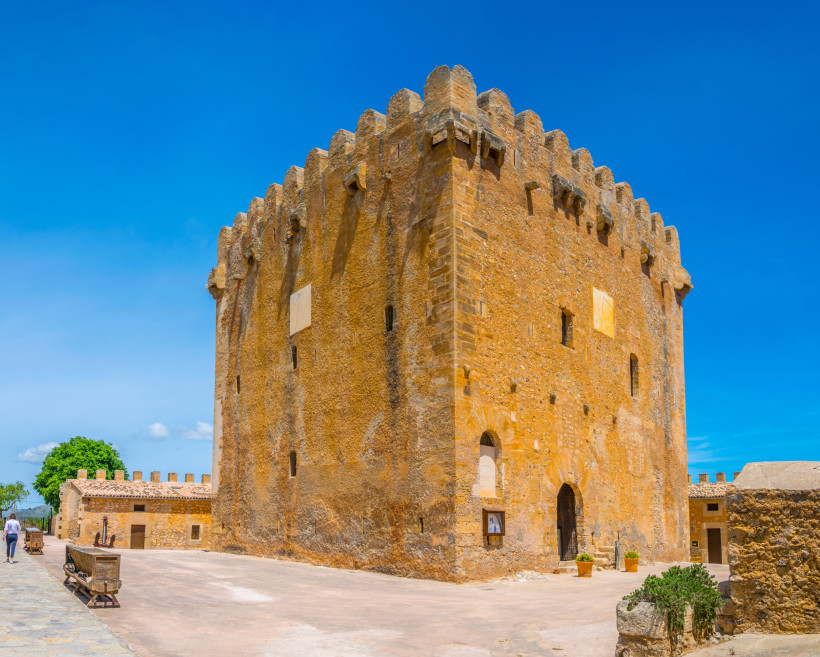 Mittelalterlicher Wehrturm Torre de Canyamel aus Naturstein mit Zinnen vor blauem Himmel