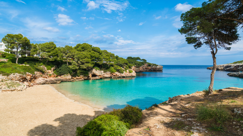 Cala d’Or Beach mit kleiner Sandbucht, Felsen und klarem Wasser im Ortsgebiet