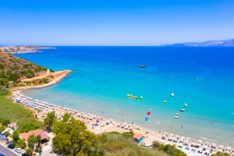 Bucht am Almyros Beach mit Sandstrand, Sonnenschirmen und ruhigem, türkisfarbenem Meer