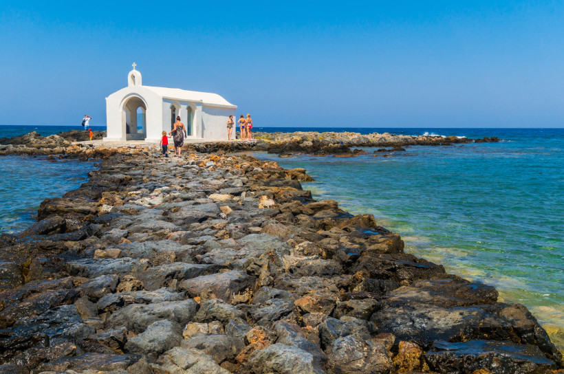 Meereskapelle Agios Nikolaos an der Küste Weiße Meereskapelle Agios Nikolaos auf einer Felseninsel, davor ein steiniger Damm im Meer