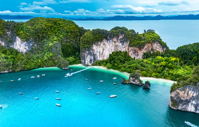 Krabi Thailand Luftaufnahme – Felsformationen, Lagunen Luftaufnahme von Krabis Küste mit steilen Kalksteinfelsen, türkisblauer Lagune und zahlreichen Booten auf dem Meer.