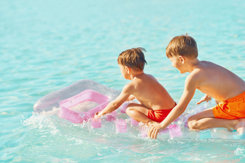 Ägypten - El Gouna Zwei Kinder in orangefarbener Badebekleidung knien fröhlich auf einer pink-transparenten Luftmatratze im flachen, türkisblauen Meer. Sie lachen, plantschen und genießen das sonnige Badevergnügen.