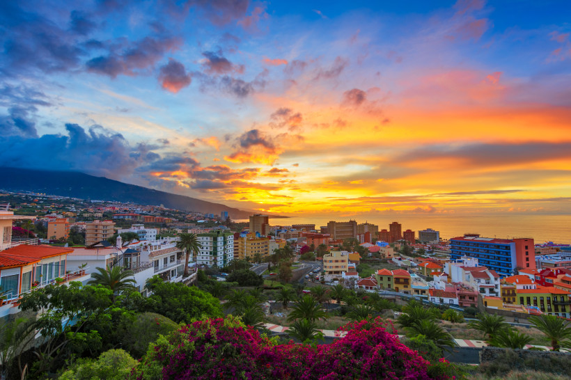 Puerto de la Cruz bei Sonnenuntergang – Farbenprächtiger Himmel über Teneriffas Norden Blick auf Puerto de la Cruz auf Teneriffa bei Sonnenuntergang mit bunten Häusern, Palmen und einem leuchtenden Himmel in Orange- und Blautönen