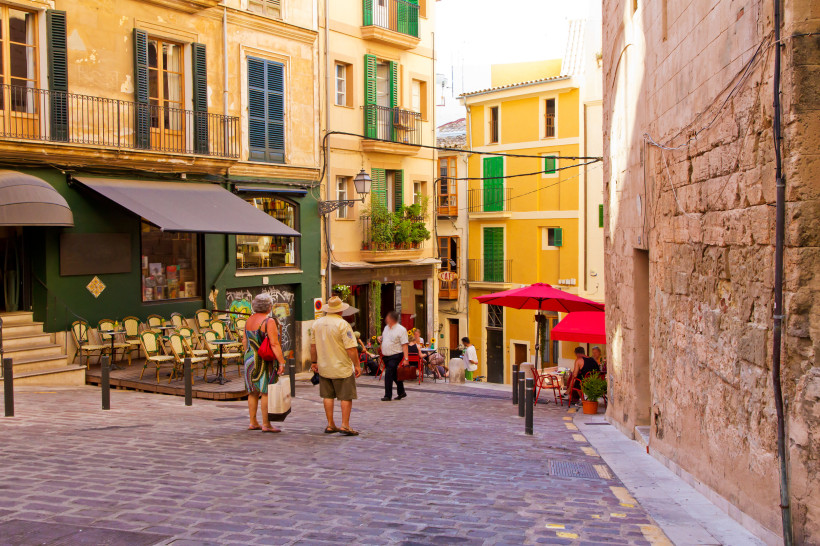 Straßenszene in der Altstadt von Palma mit Cafétischen, bunten Fassaden und Passanten