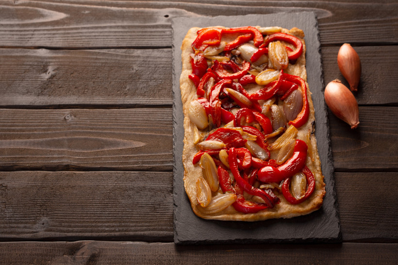 Flammkuchen mit Paprika und Schalotten auf Holzuntergrund Rechteckiger Flammkuchen mit roter Paprika und Schalotten auf Schieferplatte