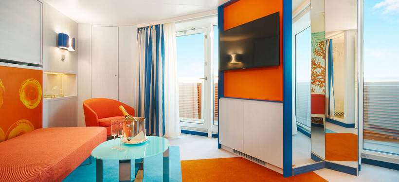 Costa Toscana Suite: Wohnbereich mit Sofa, Tisch, Fernseher und Zugang zum Balkon Wohnbereich einer Suite auf der Costa Toscana mit Sofa, Tisch, Fernseher und Balkontür