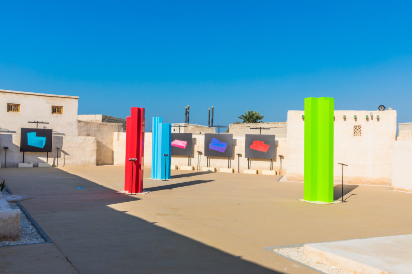 Ras al-Khaimah Art Festival Moderne Freiluft-Kunstausstellung mit bunten Skulpturen in Rot, Blau und Grün, umgeben von traditioneller sandfarbener Architektur