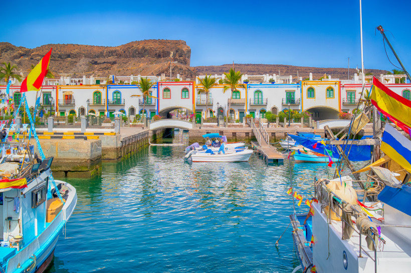 Puerto de Mogán Marina mit Booten, Brücke und bunten Häuserfassaden Marina von Puerto de Mogán mit kleinen Booten im Hafenbecken, Brücke und bunten Häuserfassaden vor felsiger Hügellandschaft