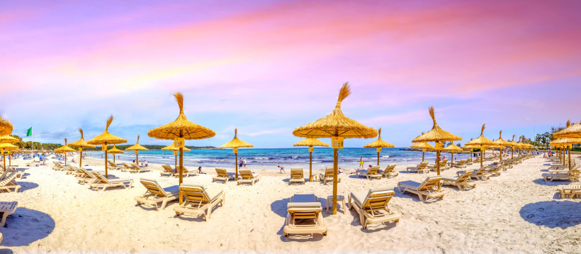 Strand von Sa Coma mit Sonnenschirmen aus Stroh und Liegen am Meer