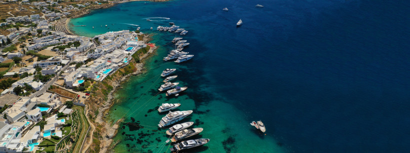 Mykonos - Psarou Beach uxusyachten vor der Küste von Mykonos, Griechenland, mit türkisfarbenem Wasser und weißen Häusern an der Bucht