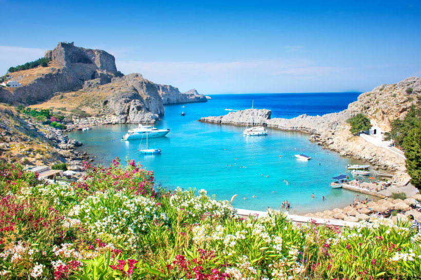 Türkisfarbene St. Paul’s Bay bei Lindos auf Rhodos mit Segelbooten, Badegästen und felsigen Klippen