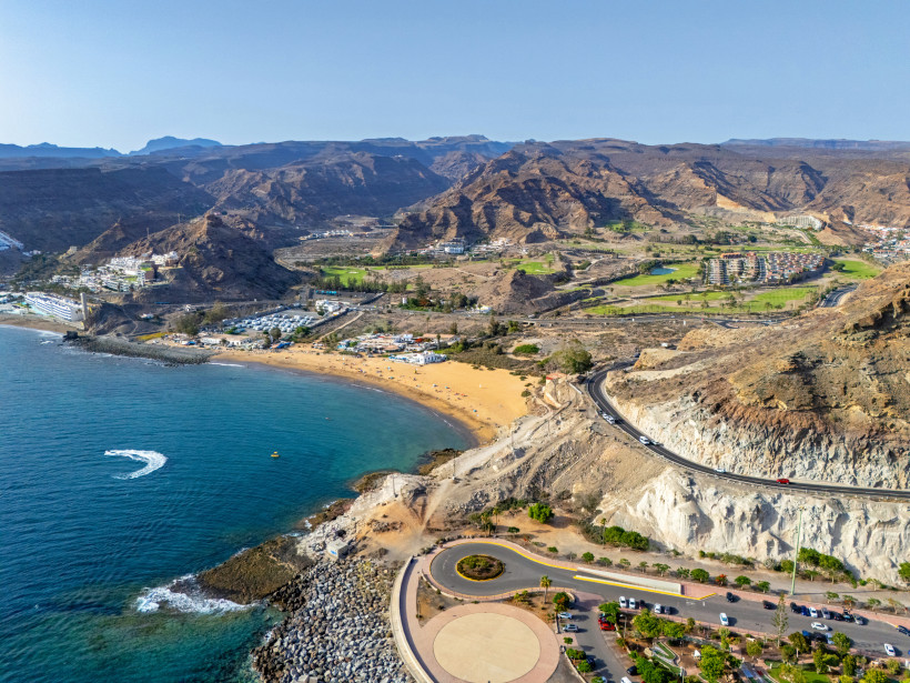 Luftaufnahme der Playa de Tauro bei Puerto Rico, Gran Canaria, mit Bucht, Sandstrand, Küstenstraße und Bergen im Hintergrund