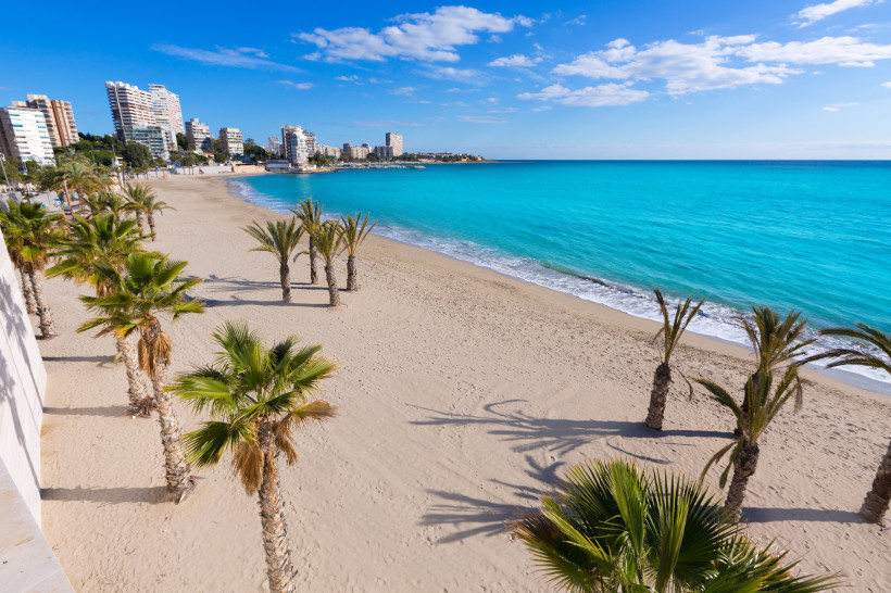 Sandstrand Albufereta in Alicante mit Palmen, Küstenbebauung und türkisfarbenem Meer