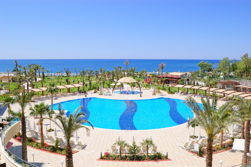 Antalya Urlaub mit Top Preis-Leistungs-Verhältnis – Pool, Strand Grosse Poolanlage eines Resorts in Antalya mit Palmen und Meerblick – steht für gutes Preis-Leistungs-Verhältnis, All-Inclusive-Urlaub und günstige Ferien an der Türkischen Riviera