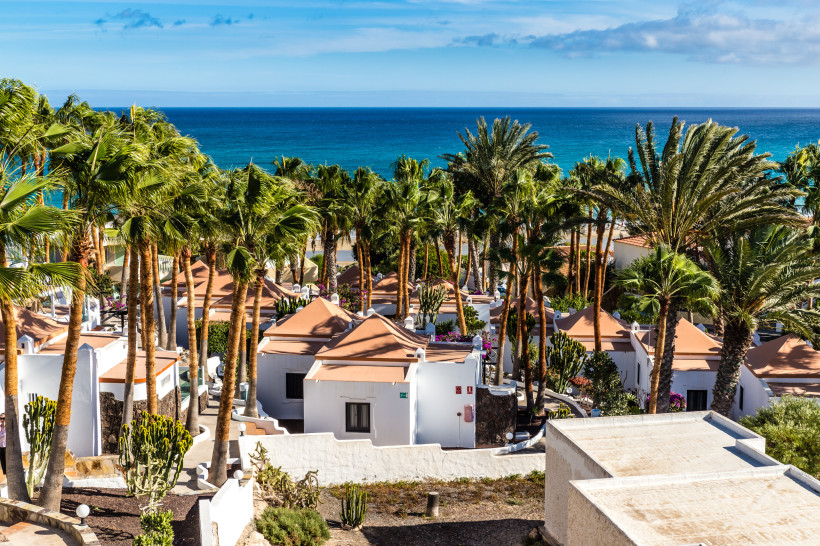 Blick auf Ferienanlage mit weißen Bungalows und Palmen an der Costa Calma auf Fuerteventura, im Hintergrund das Meer