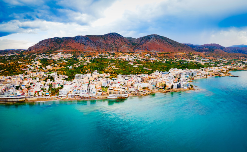 Küstenpanorama von Chersonissos mit Strandpromenade, Stadtbebauung und Bergen im Hintergrund