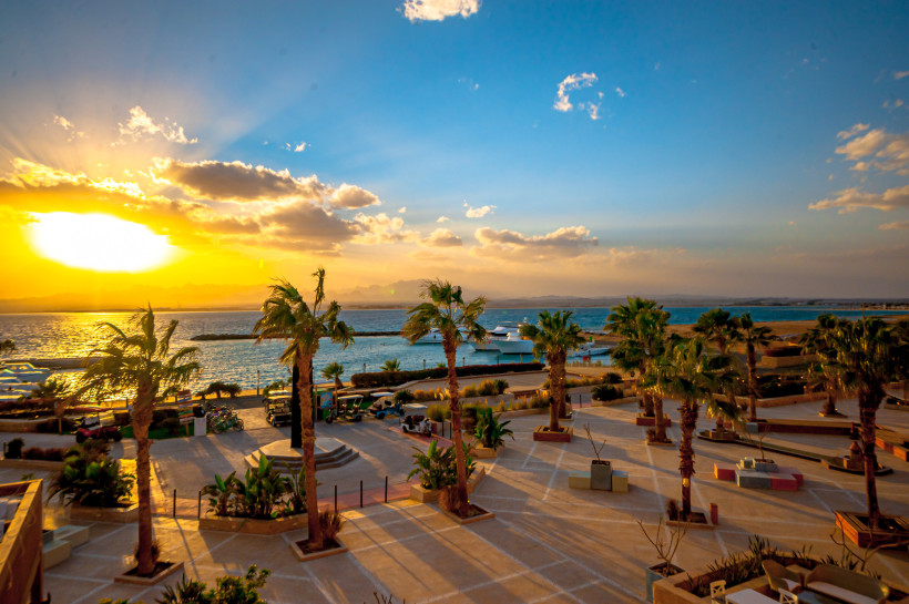 Spektakulärer Sonnenuntergang über einer palmengesäumten Hafenpromenade mit Blick auf das Meer und Boote