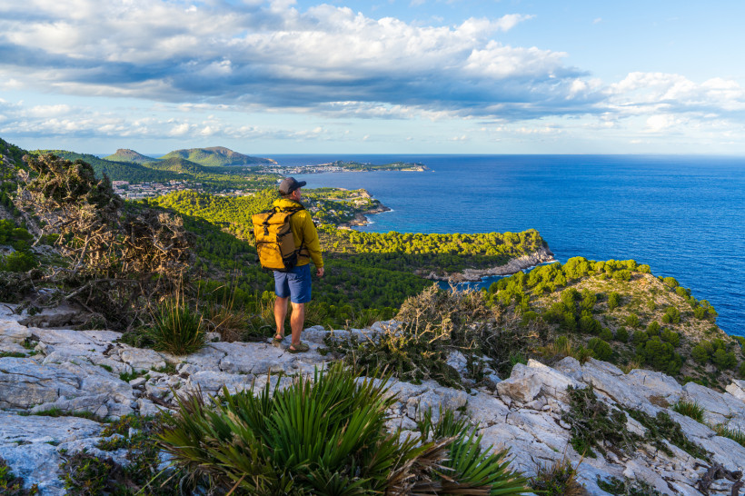 Wanderer mit Rucksack auf felsigem Aussichtspunkt über der Küste bei Canyamel