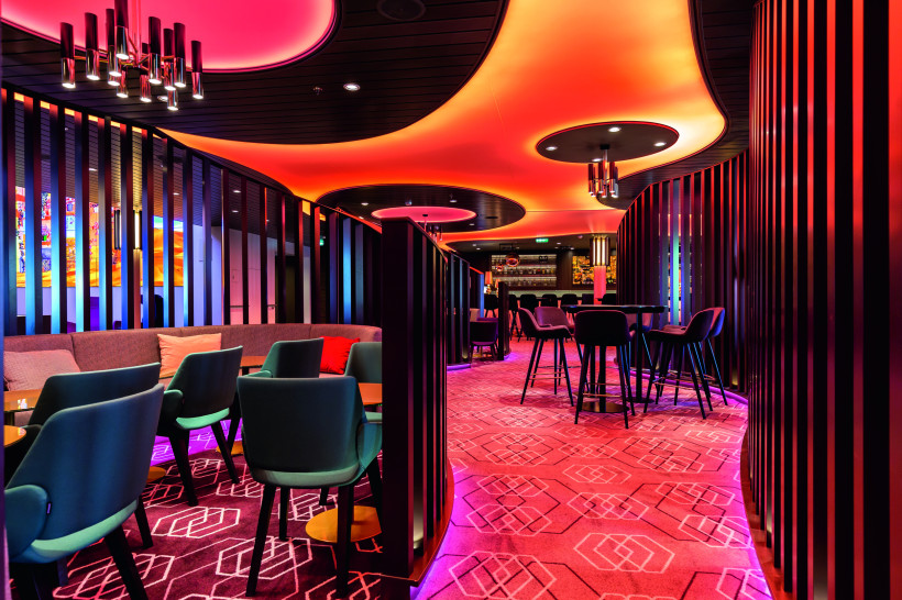 Innenansicht der LUMAS Bar auf der Mein Schiff 6 mit Sitzgruppen, Hochtischen und farbiger Deckenbeleuchtung