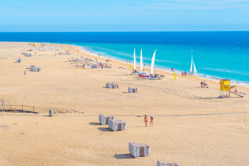 Weitläufiger Sandstrand Playa de Matorral mit Badegästen und kleinen Segelbooten am türkisblauen Meer