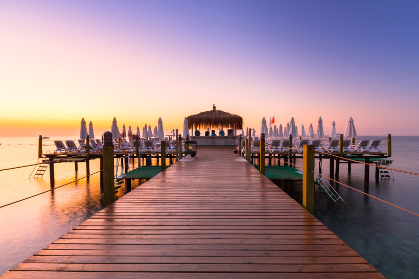 Belek Urlaub: Beste Aussichten zum besten Preis – Steg am Meer bei Sonnenuntergang Holzsteg mit Liegen und Sonnenschirmen bei Sonnenuntergang am Strand von Belek – Symbol für hohe Qualität und gutes Preis-Leistungs-Verhältnis.