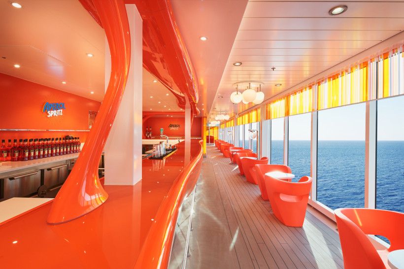 Aperol-Spritz-Bar im Innenbereich mit orangefarbenem Design und Fensterfront zum Meer Innenansicht einer Aperol-Spritz-Bar mit orangefarbener Theke, Sitzgelegenheiten und Meerblick durch große Fenster