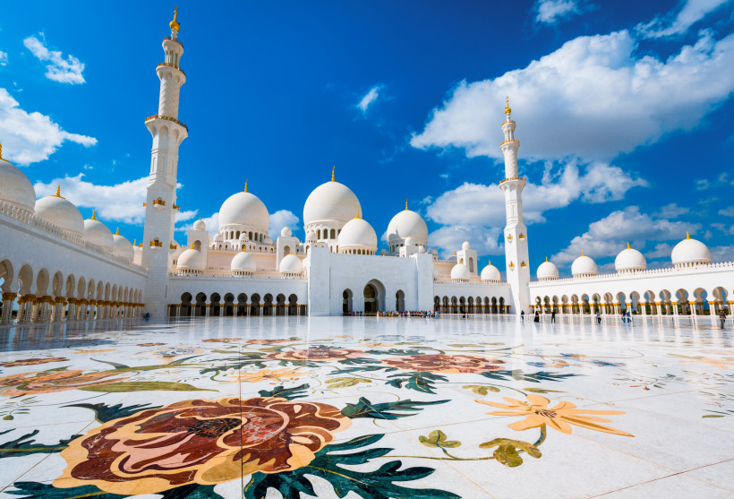 Innenhof der Sheikh-Zayed-Moschee in Abu Dhabi mit weißen Kuppeln, Minaretten und floralem Marmormosaik