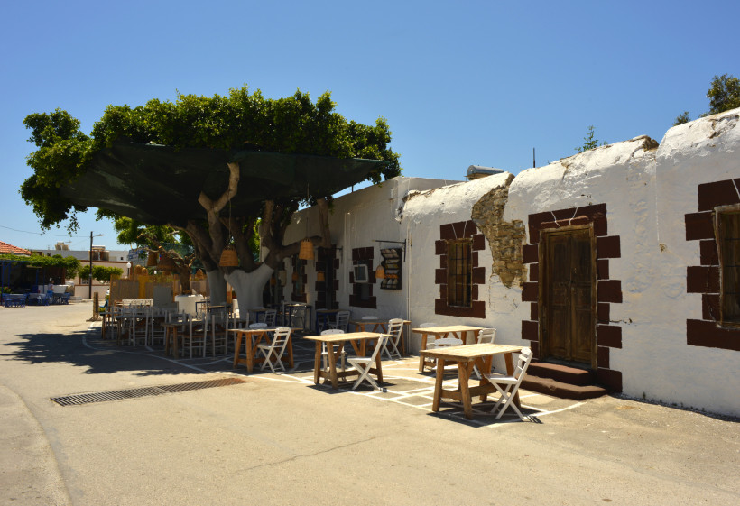 Traditionelle weiße Häuser und kleine Taverne unter einem großen Baum in einem Dorf auf Rhodos, typisch griechische Atmosphäre