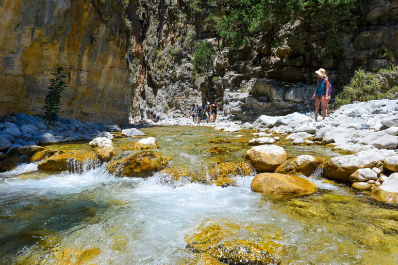 Fluss und Geröllbett zwischen steilen Felswänden in der Samaria-Schlucht Flusslauf mit Felsen und Wanderern in der Samaria-Schlucht