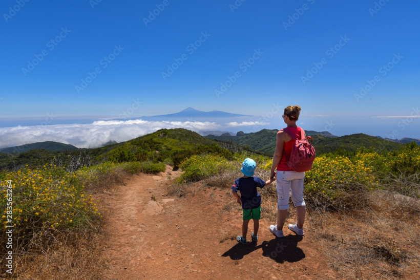 Wanderung mit Kind in den Bergen Frau und Kind auf einem Wanderweg mit Blick über bewaldete Berge, Wolkenmeer und einen Vulkan in der Ferne unter blauem Himmel
