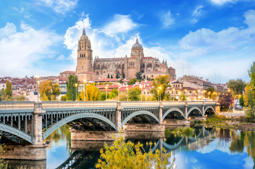 Blick auf die Kathedrale von Salamanca und eine Brücke über den Fluss Tormes bei blauem Himmel