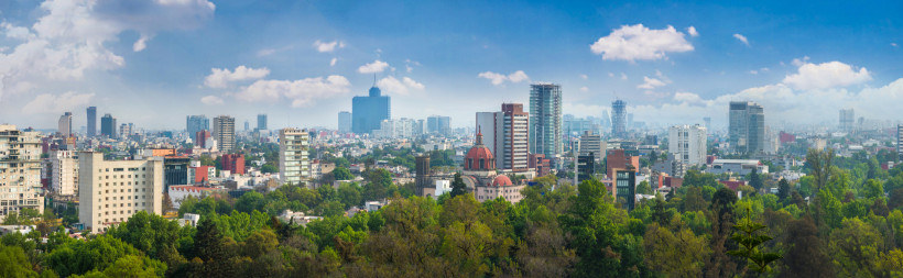 Herbst in Mexiko Panoramablick auf eine moderne Stadt mit Hochhäusern, Wohngebäuden und grünen Parks unter einem blauen Himmel mit weißen Wolken
