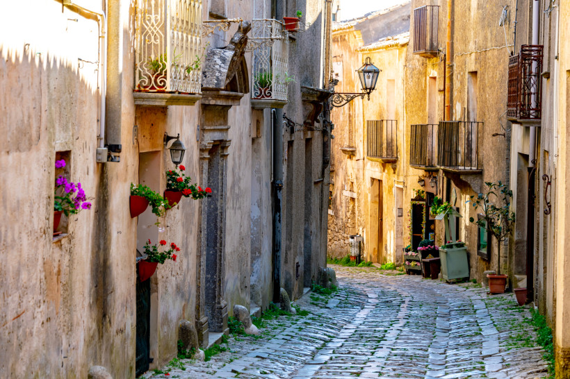 Erice – historische Altstadt mit verwinkelten Gassen auf Sizilien Malere Kopfsteinpflaster-Gasse in Erice auf Sizilien mit alten Steinhäusern, Balkonen und bunten Blumen – charmantes Bergdorf mit mittelalterlichem Flair und Panoramablick auf die Küste