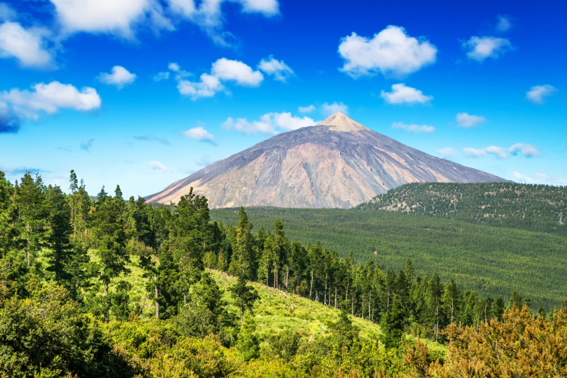 Blick auf den Pico del Teide mit bewaldeten Hängen im Vordergrund und blauem Himmel mit Wolken