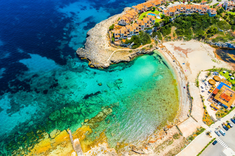Cala Murada südlich von Calas de Mallorca mit kleiner Sandbucht, türkisfarbenem Wasser und niedriger Bebauung oberhalb der Felsküste.