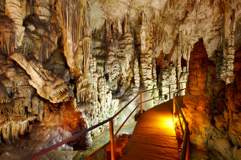 Dikteon-Höhle: beleuchteter Steg zwischen Tropfsteinformationen Holzsteg in der Dikteon-Höhle mit Stalaktiten und Stalagmiten