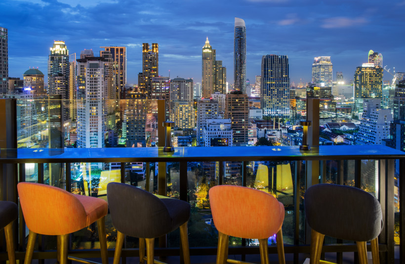 Stylische Rooftop-Bar mit Panorama-Ausblick auf die Skyline von Bangkok bei Nacht Moderne Rooftop-Bar mit stilvollen Stühlen und spektakulärem Blick auf die beleuchtete Skyline von Bangkok