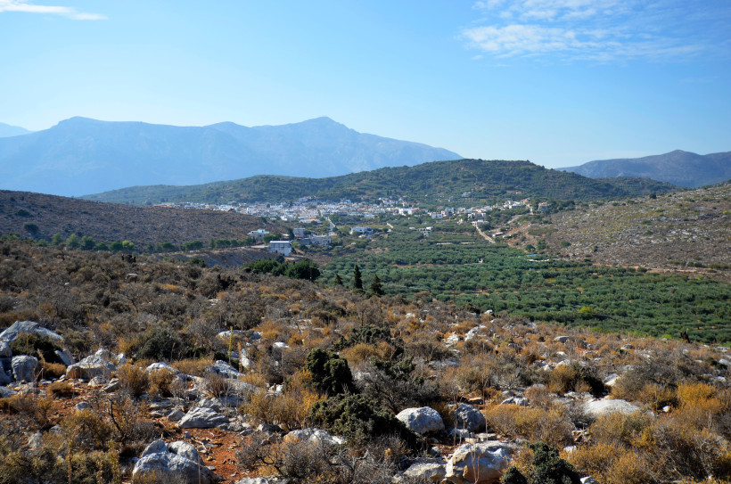Blick auf das Bergdorf Mochos mit Olivenhainen und Bergkulisse Bergdorf Mochos in einem Tal mit Olivenhainen, umgeben von Hügeln und Bergen