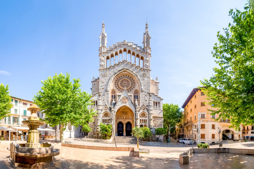 Plaça de la Constitució mit Kirche, Brunnen und Bäumen bei Sonnenschein