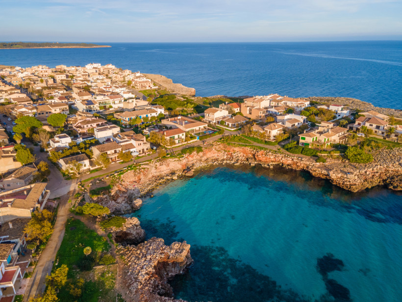 Luftaufnahme von S’Illot mit Häusern an der felsigen Küste und türkisblauer Bucht