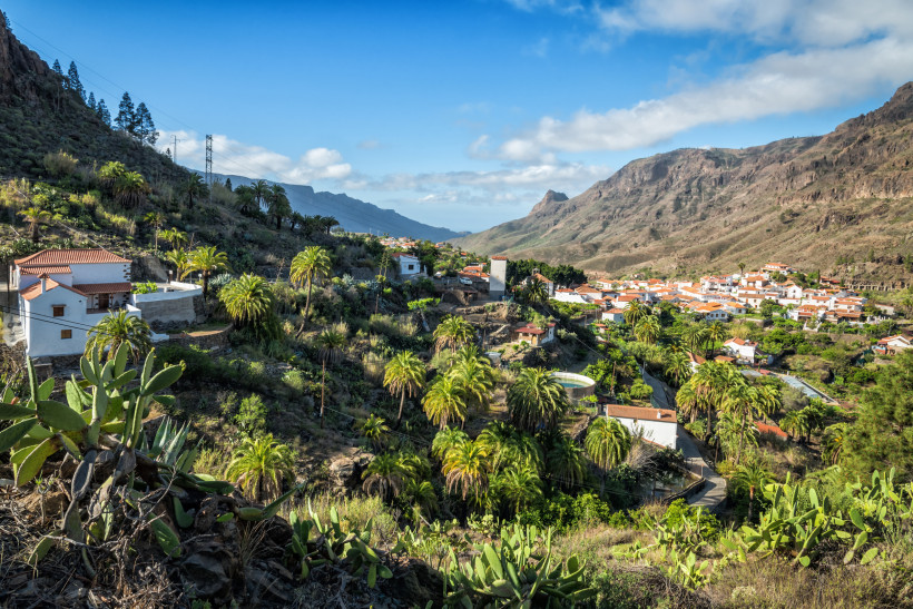 Blick auf das Bergdorf Fataga auf Gran Canaria mit weißen Häusern, roten Ziegeldächern, Palmen und umgebenden Bergen.