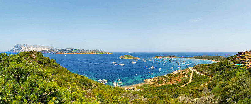 Panoramablick über Porto San Paolo auf Sardinien mit Yachten in der Bucht, grüner Küstenlandschaft und der vorgelagerten Insel Tavolara im Mittelmeer