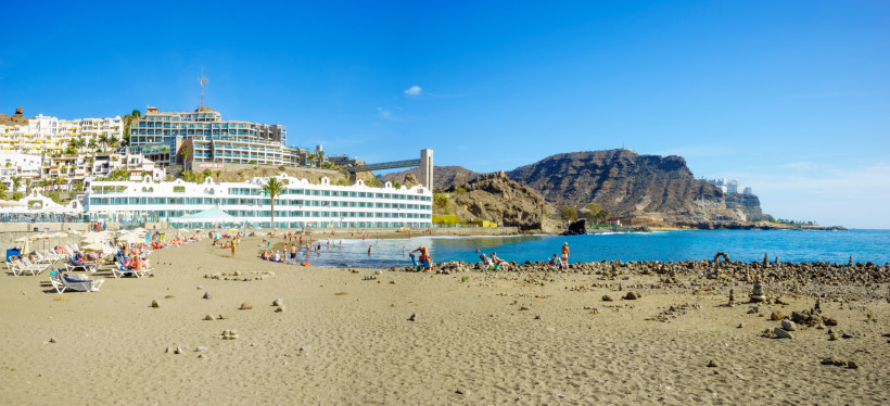 Strand Playa del Cura bei Puerto Rico, Gran Canaria, mit Hotelanlagen, Badegästen und Felsküste